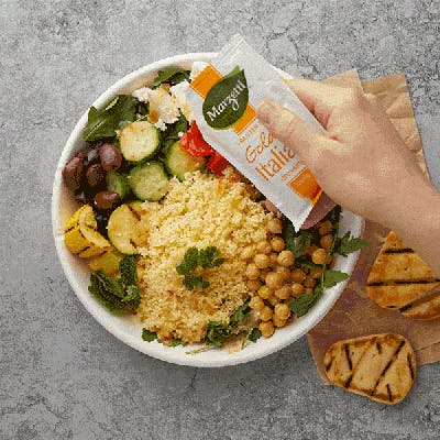 Top down view of someone using a dressing packet to add dressing to their salad